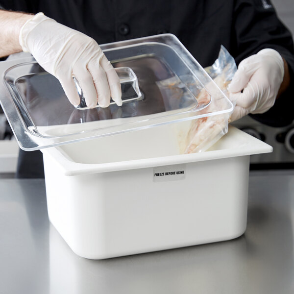 A person in gloves and a white apron putting a Carlisle plastic lid on a food container.