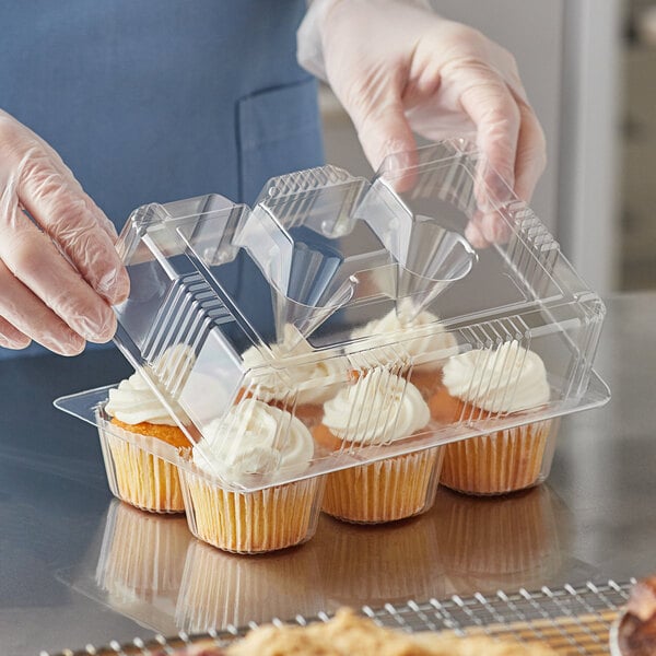 A person in gloves placing a frosted cupcake in a Choice plastic container.