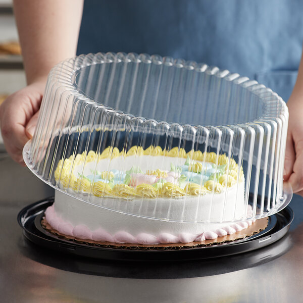 A person holding a Choice plastic dome lid over a frosted cake in a plastic container.