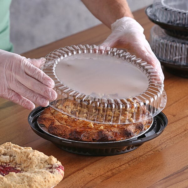 A person in gloves holding a Choice black plastic pie container with food inside on a counter.
