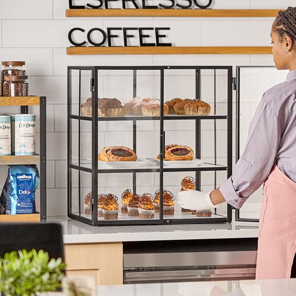 A three-tier bakery display case with a black frame and glass panels, containing assorted pastries.