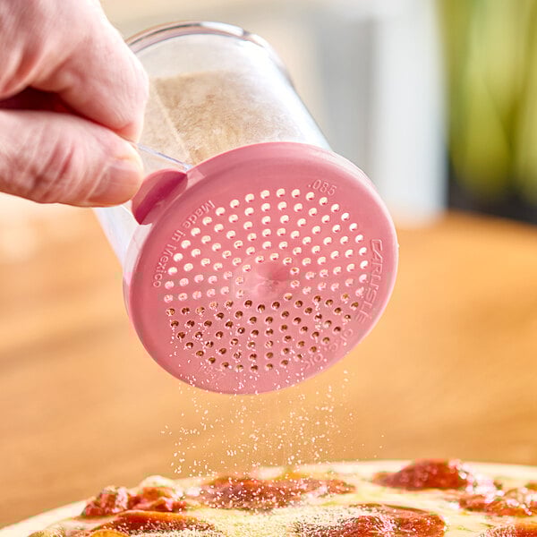 A person using a Carlisle polycarbonate shaker with a pink rose lid to pour powder onto a pizza.