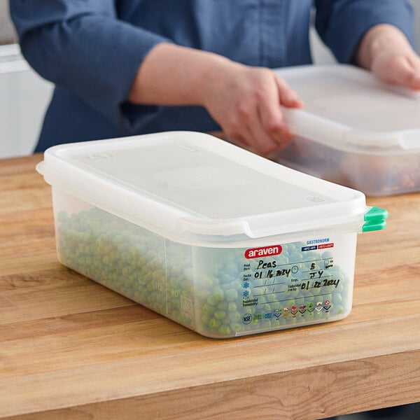 A person holding a Araven translucent plastic food pan filled with green peas.