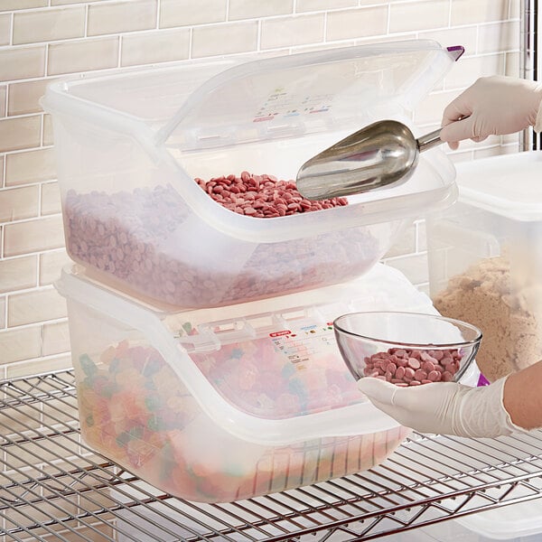 A hand using a silver scoop to add pink ingredients from an Araven shelf ingredient bin to a bowl of food.