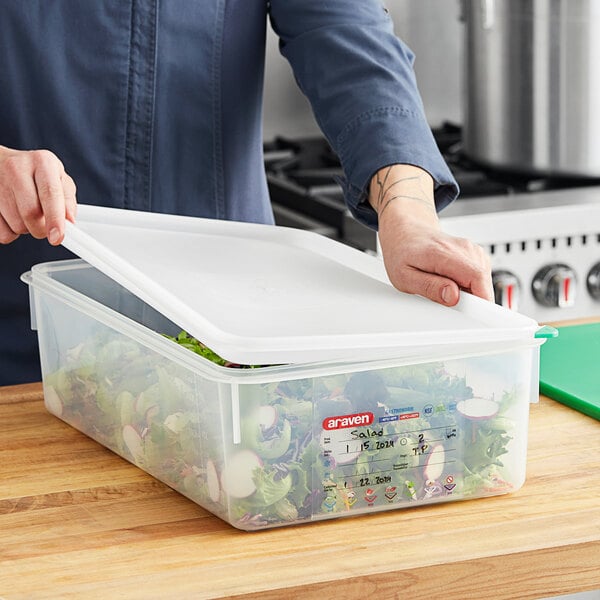 A person holding a Araven translucent polypropylene food pan with a lid full of salad.