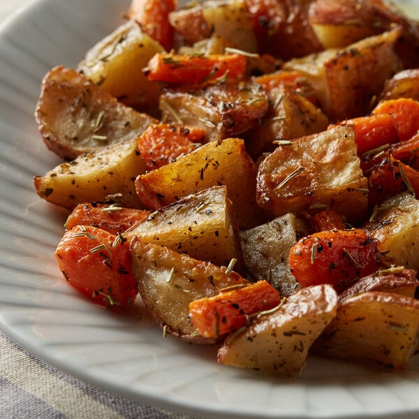 A plate of food on a table with rosemary on potatoes and carrots.