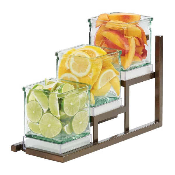 A Cal-Mil Sierra Bronze 3 step jar display with fruit in glass containers.
