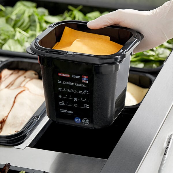 A hand in a glove holding a black container of food.