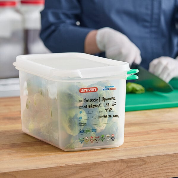 A woman in blue gloves cutting vegetables in a translucent Araven plastic food pan on a counter.
