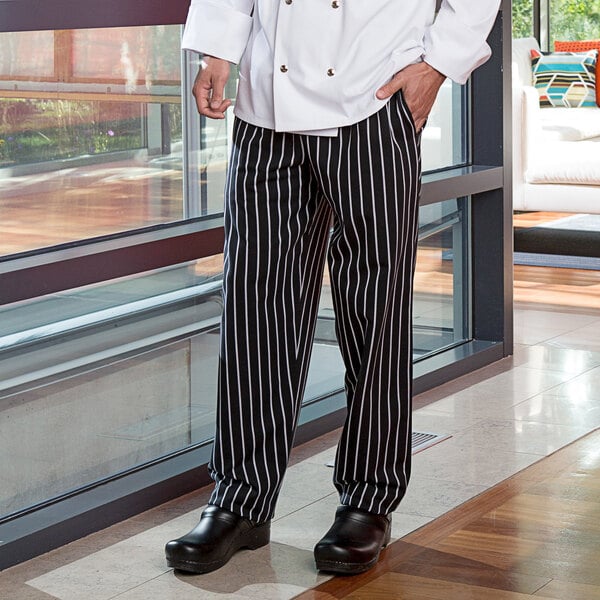A man wearing Uncommon Chef black and white striped pants in a professional kitchen.