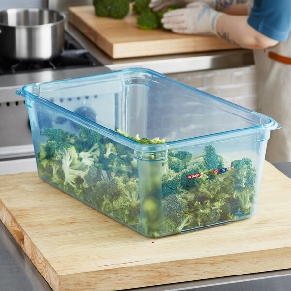 A woman in a blue shirt and gloves cutting broccoli in a blue Araven plastic container.