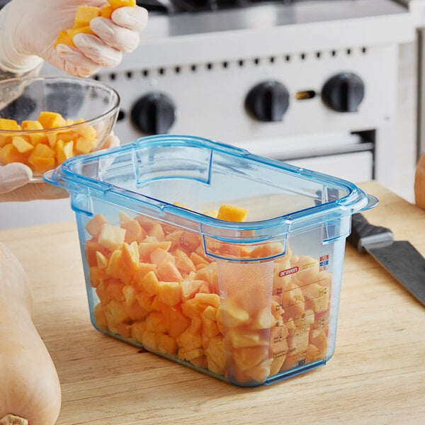 A person using a knife to cut oranges into a blue Araven plastic food container.