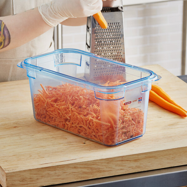 A person grating carrots in a blue Araven plastic food pan.
