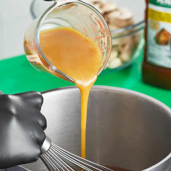 A close-up of a measuring cup with orange liquid being poured into a bowl of Knorr Ultimate Liquid Concentrated Chicken Base.