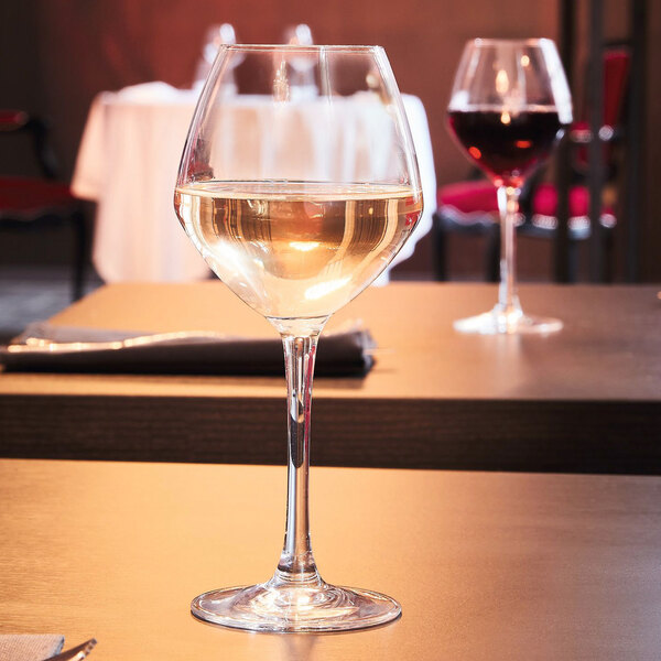 A glass of white wine on a table with a wine glass.