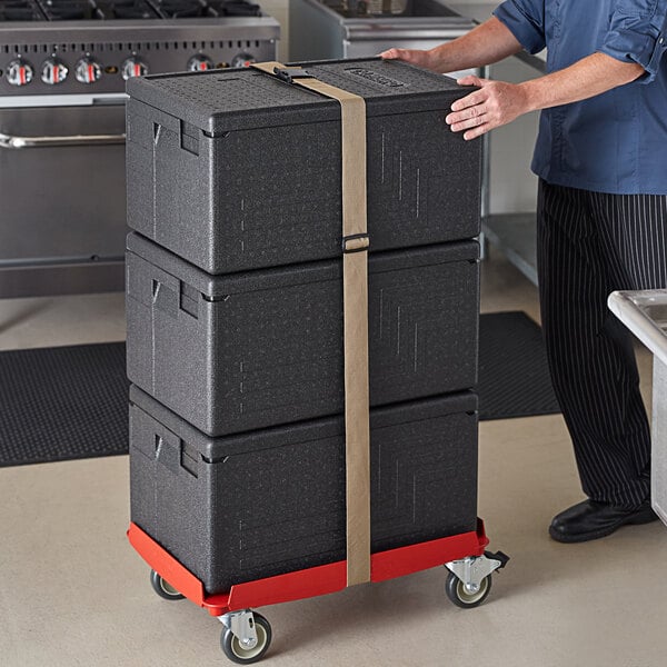 A man pushing a stack of black Cambro Cam GoBox pan carriers on a black Compact Camdolly.