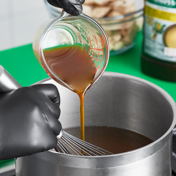 A person pouring brown Knorr liquid into a pot.