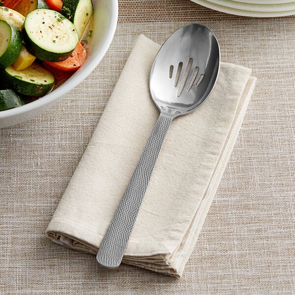 A white bowl of vegetables with a vintage stainless steel slotted spoon on a napkin.