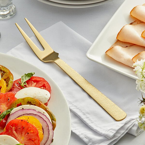 An American Metalcraft hammered gold cold meat fork next to a plate of vegetables on a table.