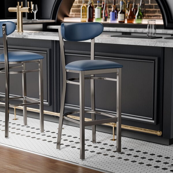 Two Lancaster Table & Seating navy vinyl bar stools with a clear coat finish at a black bar counter.