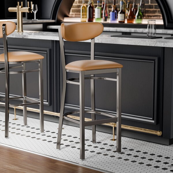 Two Lancaster Table & Seating bar stools with light brown vinyl seats and backs at a bar counter.