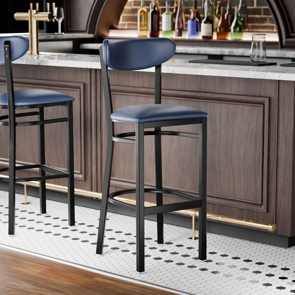 A black bar stool with a navy vinyl seat and backrest, positioned at a bar counter.