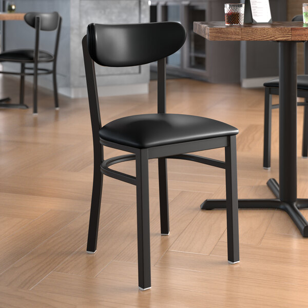 A black Lancaster Table & Seating Boomerang Series chair with black vinyl seat and back next to a table in a restaurant.