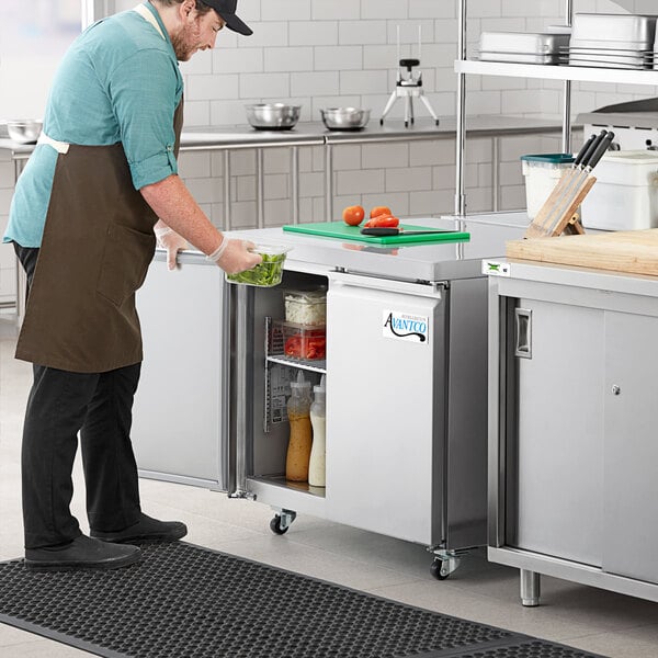 A man in a kitchen putting food in an Avantco undercounter refrigerator.