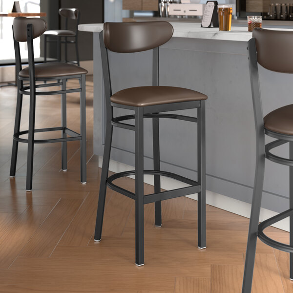 Three Lancaster Table & Seating black bar stools with dark brown vinyl seats and backs at a kitchen counter.