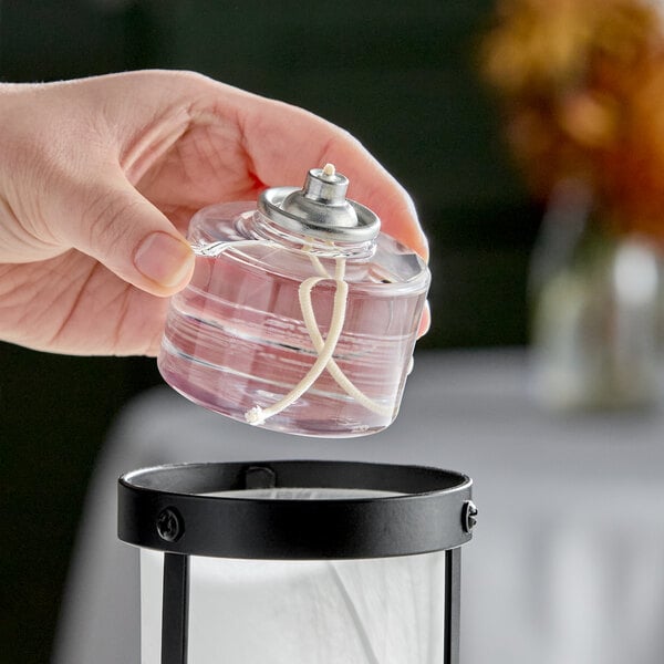 A clear liquid candle fuel cartridge with a visible wick being placed into a lantern.