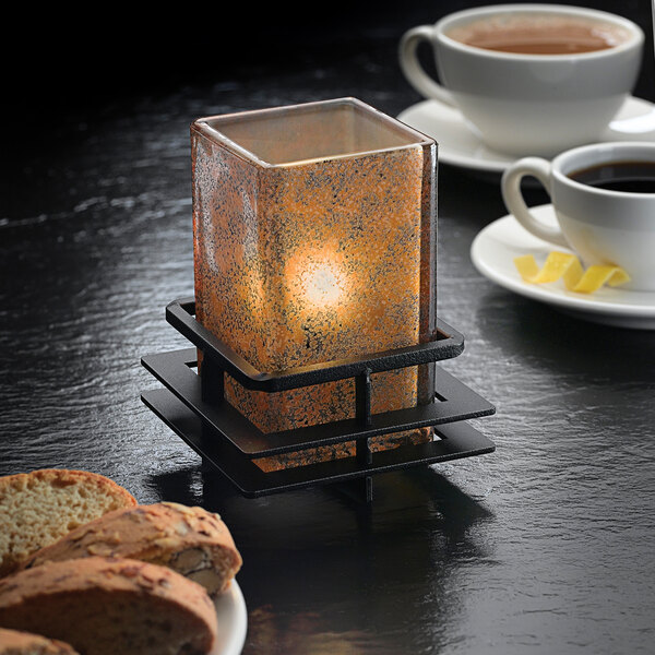 A Hollowick Craftsman black low iron candle holder with a lit candle next to a plate of coffee and cookies.