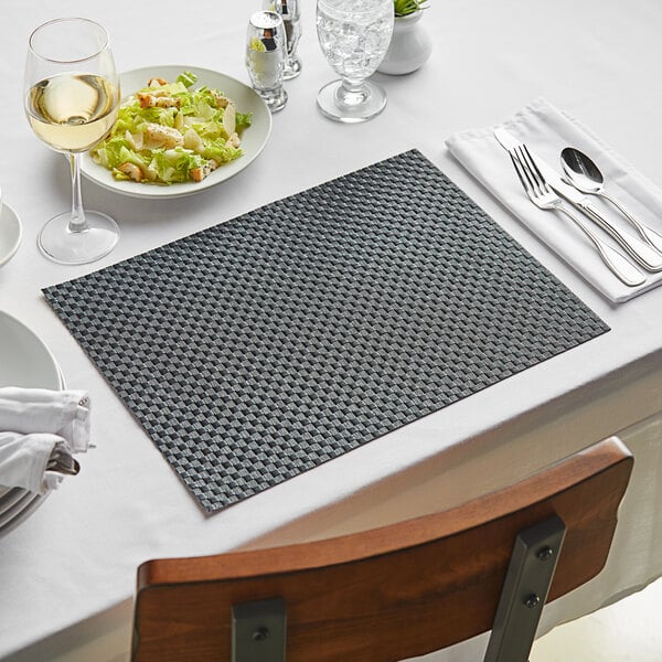 A table set with black woven vinyl rectangle placemats, white plates, and silverware.