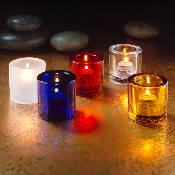 A group of Hollowick clear glass tealight candles in different colors on a table.