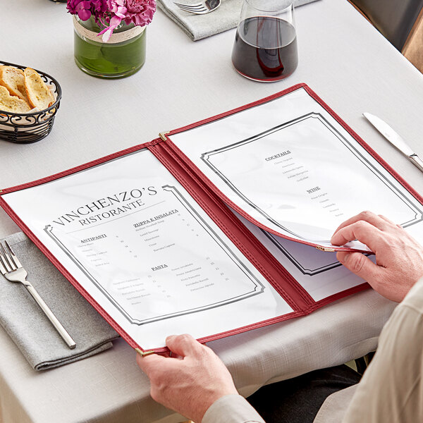 A person holding a red H. Risch, Inc. menu cover with gold corners on a table.