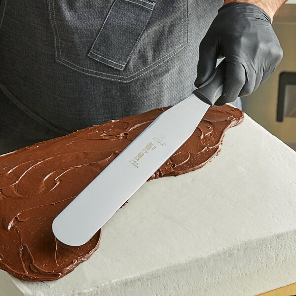 A person using a Dexter-Russell V-Lo straight baking spatula to cut a cake.