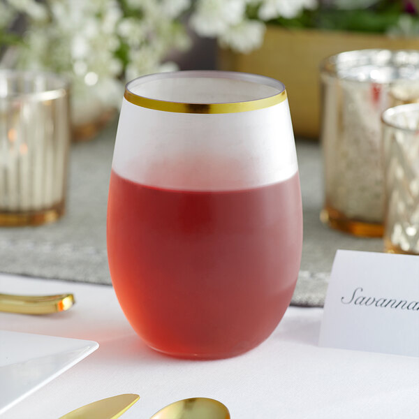 A Visions clear plastic stemless wine glass with a gold rim full of red liquid on a table.