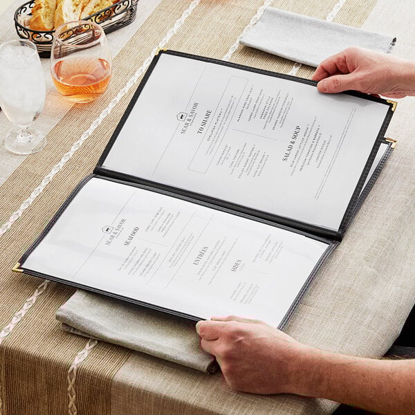 A person opening a black rectangular menu with gold corners.