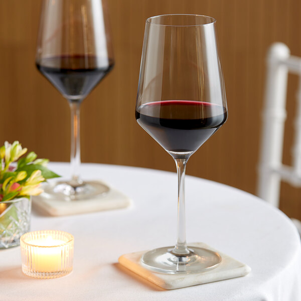 Two Zwiesel Glas Pure Cabernet wine glasses filled with red wine on a table with a candle.