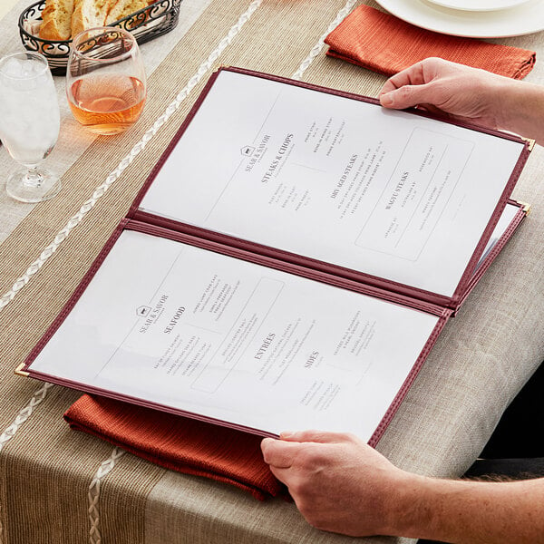 A person holding a H. Risch, Inc. maroon menu on a table.