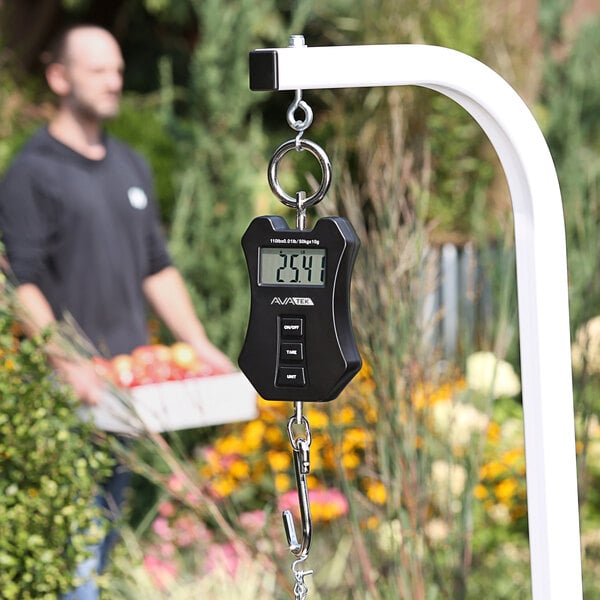 A man holds a black AvaWeigh digital hanging scale.