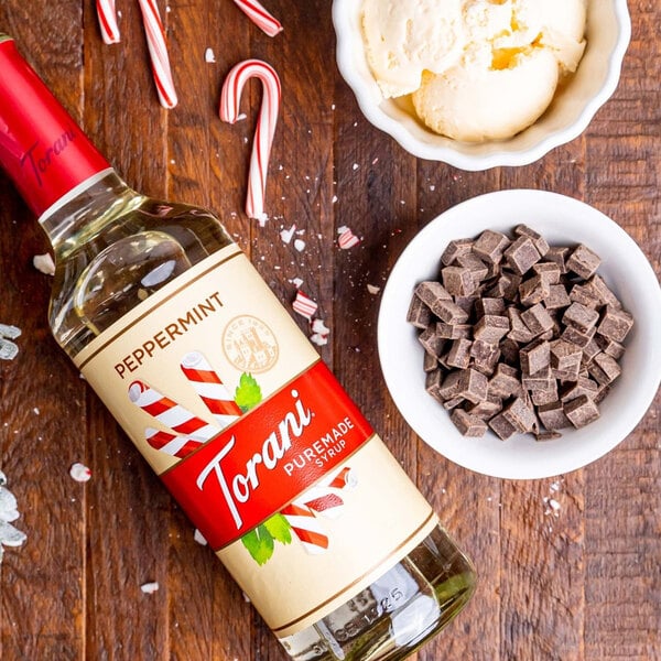 A bottle of Torani Puremade Peppermint flavoring syrup next to a bowl of candy canes and a bowl of chocolate cubes.