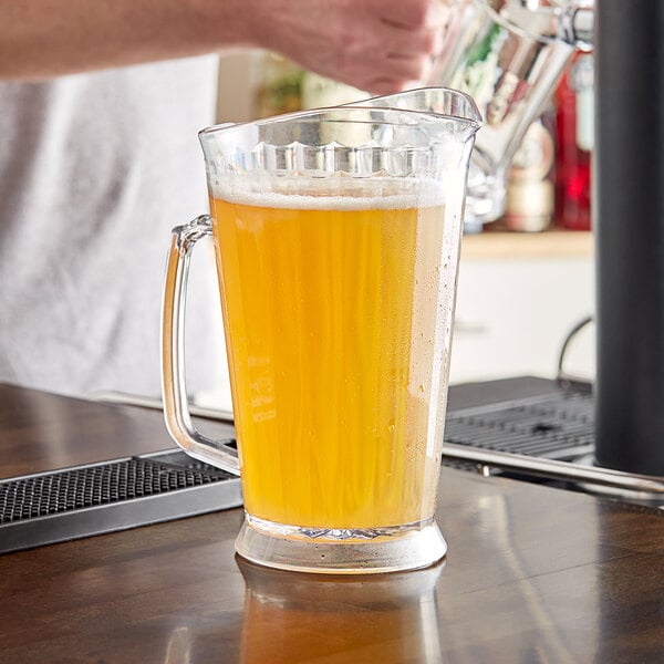 A person pouring a liquid into a Carlisle Clear Polycarbonate Beverage Pitcher.