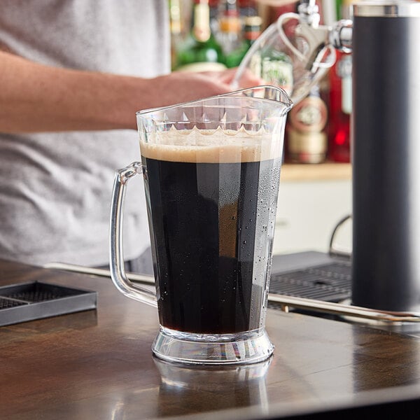 A man pours dark liquid into a Carlisle Clear Polycarbonate Beverage Pitcher.