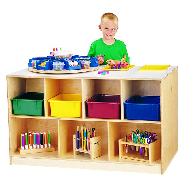 A young boy standing in front of a Jonti-Craft wood storage island with clear plastic tubs.