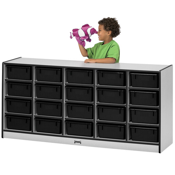 A young boy standing in front of a Rainbow Accents mobile storage cabinet with black bins.