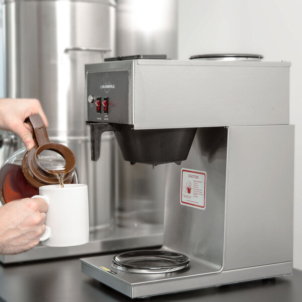 A person pouring coffee into a Bloomfield commercial coffee maker.