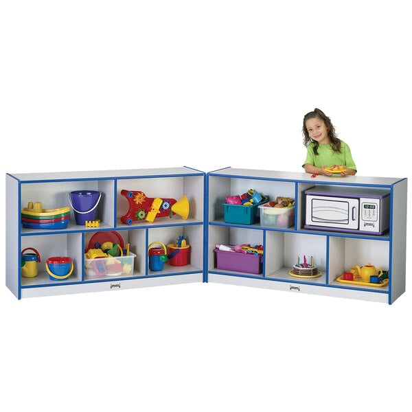 A little girl standing in front of a Rainbow Accents blue and gray storage cabinet filled with toys.