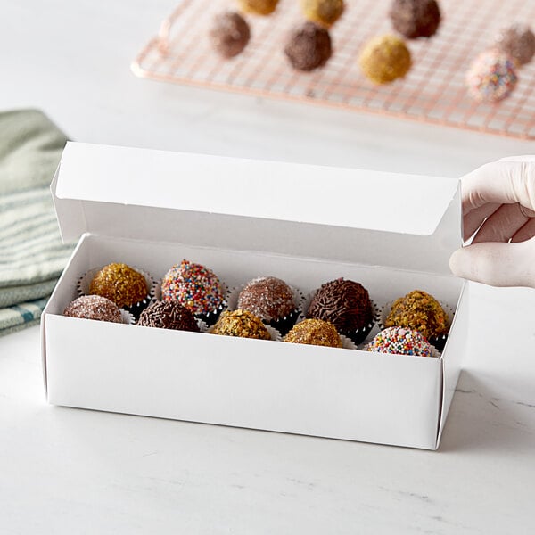 A hand holding a white 2 lb. candy box filled with chocolate truffles.