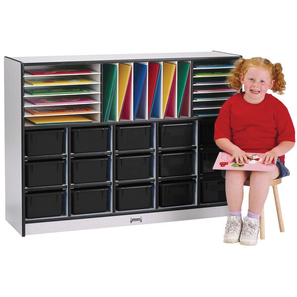 A girl sitting on a stool with a Rainbow Accents black storage cabinet full of books.