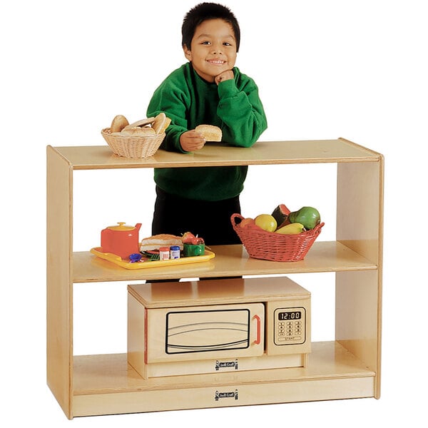 A young boy standing in front of a Jonti-Craft children's wooden shelf.